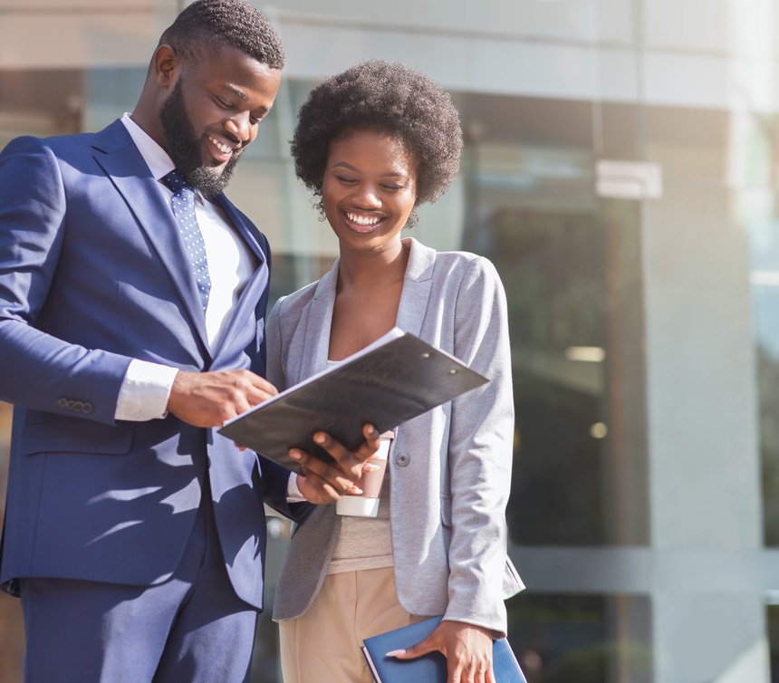 Happy couple of african american business partners working while standing outdoors, discussing new project. Blurred background with copy space